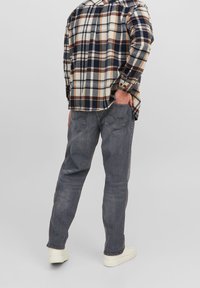 Šedé džínové kalhoty s rovnými nohavicemi, doplněné kostkovanou flanelovou košilí v béžové, námořnické modři a hnědé, viděné ze zadu.