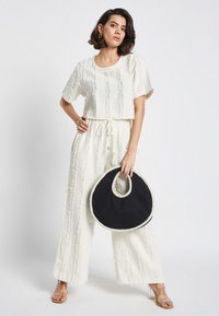 Weißes, strukturiertes Zweiteiler-Outfit mit kurzen Ärmeln und Kordelzugbund, kombiniert mit einer schwarzen runden Tasche mit einem Ausschnitt-Griff.