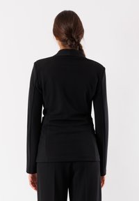 Giacca nera su misura a maniche lunghe con una forma aderente, texture liscia e colletto a rever. Design minimalistico, senza motivi o accenti visibili.