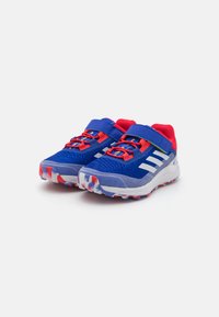 Blue athletic shoes with red accents, mesh upper, Velcro strap, white stripes, and a colorful, textured rubber outsole for grip.