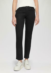 Jeans negros de corte slim, fabricados en denim. Presentan un cierre de botón, bolsillos frontales y una textura suave. Combinados con zapatillas de plataforma blancas.
