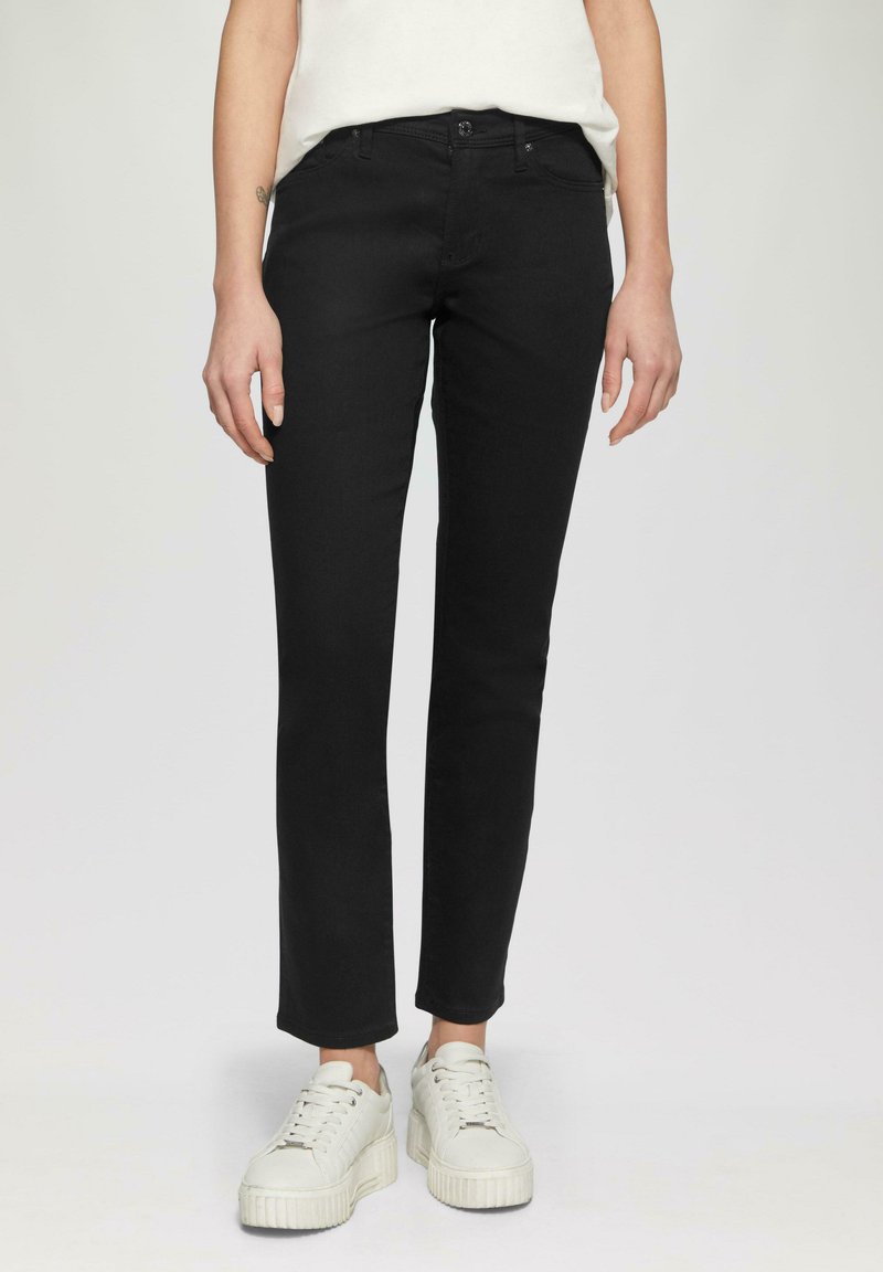 Jeans negros de corte slim, fabricados en denim. Presentan un cierre de botón, bolsillos frontales y una textura suave. Combinados con zapatillas de plataforma blancas.
