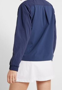 Person wearing a navy blue long-sleeve jacket and a white checkered skirt, shown from the back against a plain background.