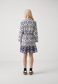 Rochie cu model floral în alb și bleumarin, având mâneci lungi, talie elastică și tiv volanat. Purtați-o cu șosete și pantofi negri.