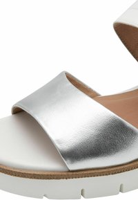Sandalo slide metallico argento con fascia larga, suola bianca e plantare testurizzato. Il design presenta un'estetica minimalista e materiali morbidi.