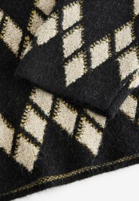 Couverture en laine noir et crème avec des motifs en diamant. Présente une texture douce et des couleurs contrastées, bordée d'un subtil fil jaune.