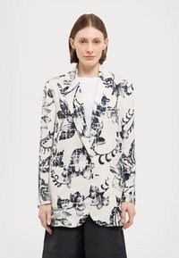 Hvid blazer med sort blomsterprint, spids krave, enkelt knaplukning og to frontlommer. Glat tekstur og struktureret design.