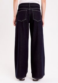 Mørkeblå brede jeans lavet af denim, med h�øj talje, hvid syning og to baglommer; glat tekstur med kantede kanter.