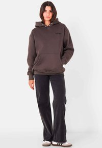 Hoodie surdimensionné gris foncé avec une poche avant et un capuchon à cordon. Associé à un jean larges noirs et des baskets claires.