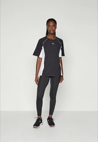 Zwart-wit sportt-shirt met korte mouwen, gecombineerd met zwarte leggings en zwarte sneakers met roze accenten.