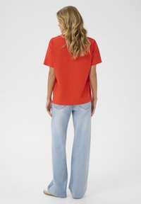 Haut rouge à manches courtes associé à un jean à jambes larges bleu clair, présentant une coupe décontractée et une texture en coton doux avec une finition lisse.