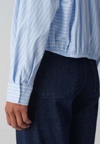 Camicia a righe celesti con orlo elastico e polsini con bottoni, abbinata a jeans in denim scuro con tasche posteriori e una vestibilità aderente.
