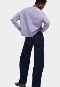 Maglione corto color lavanda con polsini e orlo a costine, abbinato a jeans in denim scuro a vita alta con tasche posteriori e cuciture a contrasto.