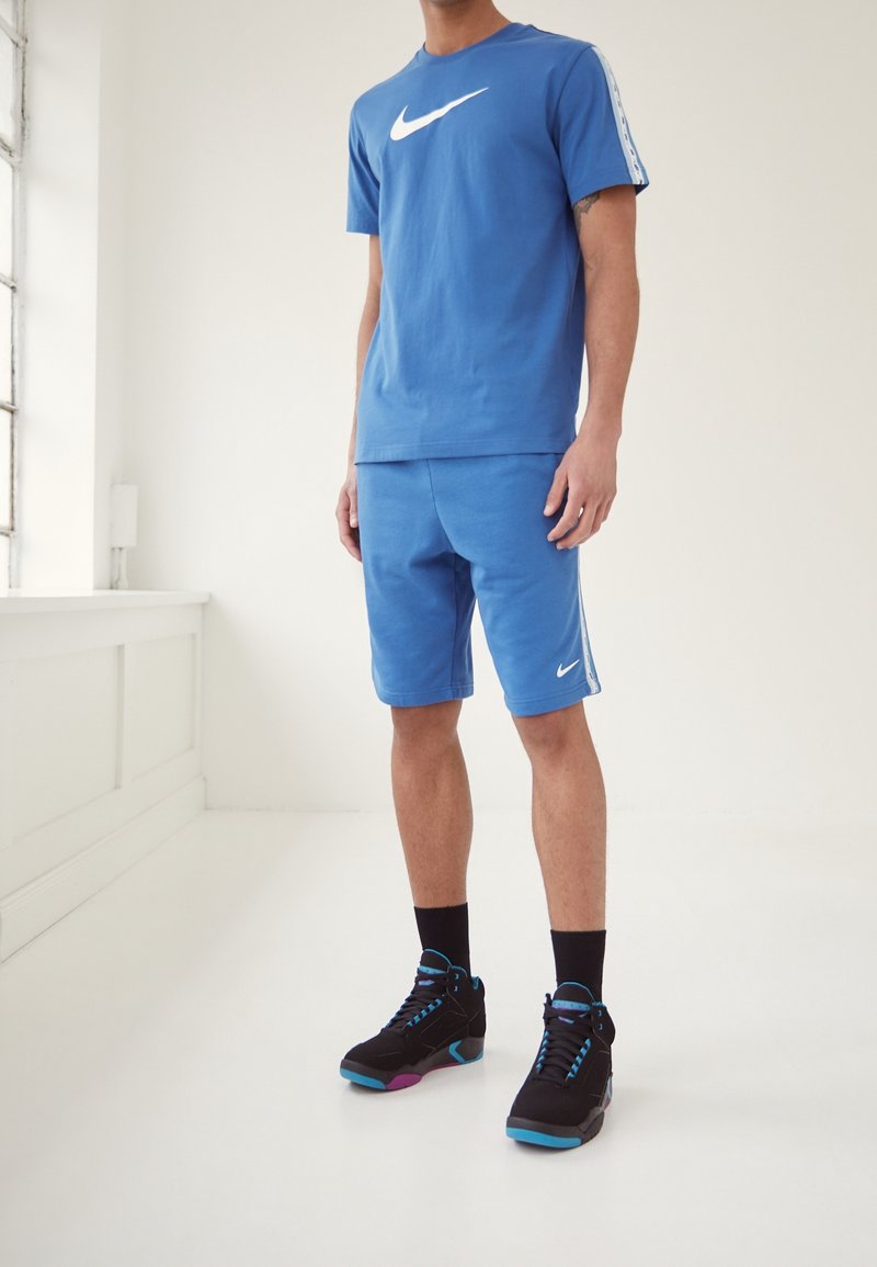 Camiseta azul de Nike con logo blanco, combinada con pantalones cortos azules a juego. Zapatillas negras con detalles en azul y rosa. Diseño sencillo, material de algodón.
