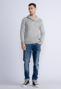 Pulover gri din tricot cu un guler tip șal, detaliu cu nasturi, asortat cu blugi albaștri și adidași negri cu gât înalt.