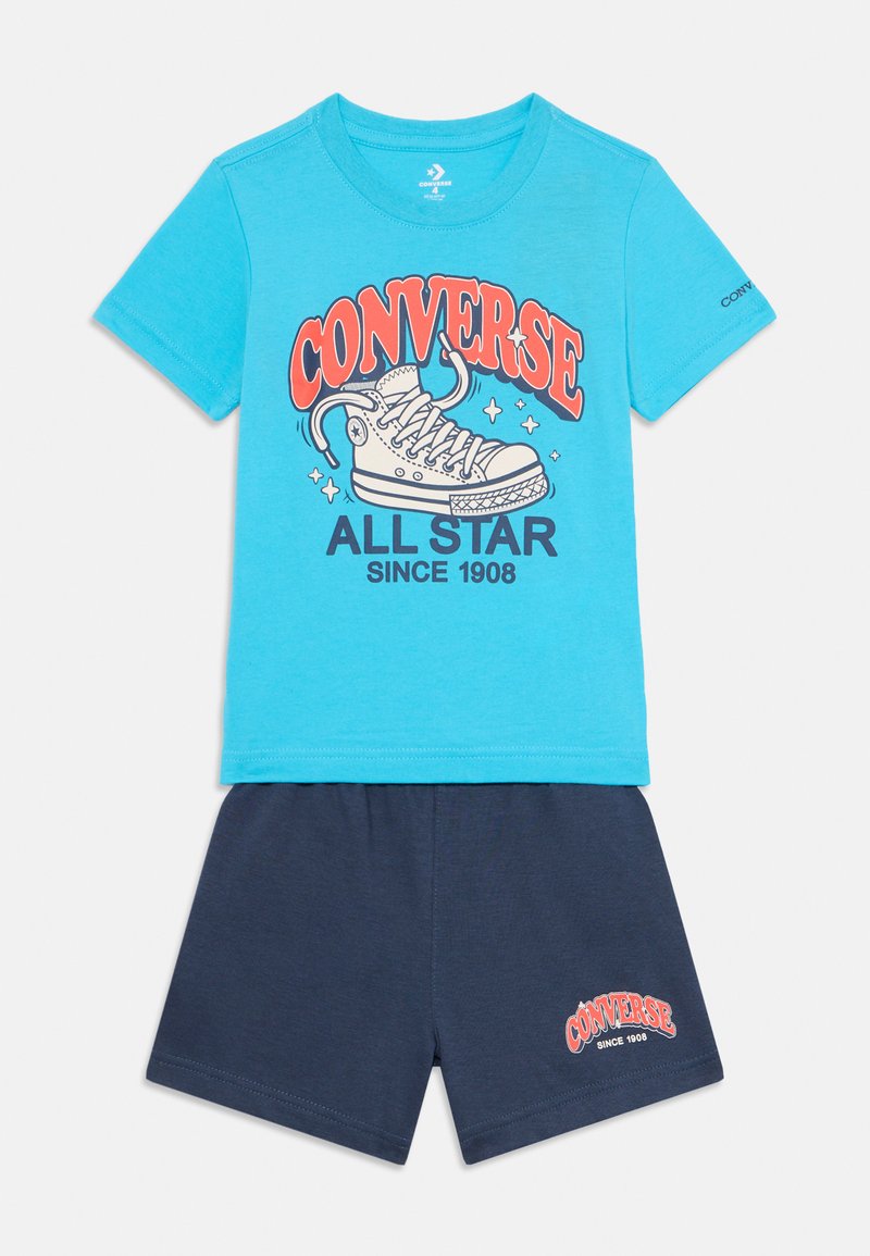 Blå bomullströja med grafiken "CONVERSE ALL STAR" och vit sneakersdesign; kombinerad med marinblå shorts med en liten logotypdetalj.