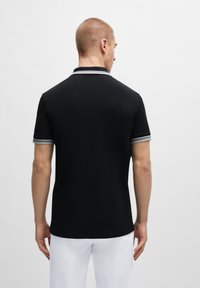 Polo noir en tissu texturé, à manches courtes avec des accents rayés gris et blancs aux poignets et un dos épuré.