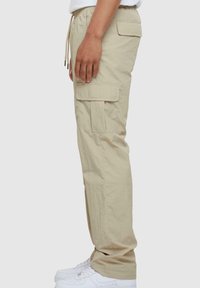 Beige cargobroek met een drawstring taille, zijzakken en een ontspannen pasvorm. Gemaakt van lichtgewicht stof, goed te combineren met witte sneakers.