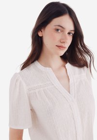 Witte blouse met korte pofmouwen, geweven stof met verticale strepen en kleine stippenpatronen, V-hals met kantdetails.