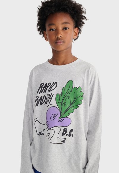 Young person wearing a light gray sweatshirt with a cartoon purple radish, green leaves, and text "Rapid Radish B.C." on a plain background.