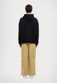 Felpa nera con cappuccio e vestibilità rilassata, abbinata a pantaloni cargo beige a gamba larga con molteplici tasche e polsini con cordoncino.