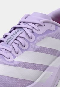 Gaiši purpursarkans skriešanas apavs ar baltām svītrām, teksturētu auduma virsu un plakaniem šņorēm. ADIZERO zīmols uz mēles. Vieglas konstrukcijas.