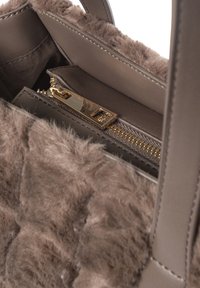 Sac à main marron avec un extérieur en fourrure texturée, comprenant une poche zippée, un intérieur en cuir lisse et des accents en métal doré.