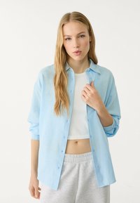 Light blue button-down shirt in soft fabric with long sleeves, worn over a white crop top and paired with gray sweatpants.