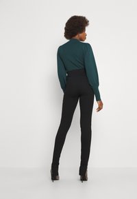 Camisola de manga longa em tom de verde-água, com textura canelada e decote redondo, combinada com leggings pretas de cintura alta e sapatos de salto altos cinzas.