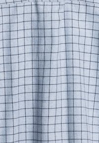 Lichtblauwe stof met een ruitpatroon in donkerder blauw. De textuur lijkt zacht, met subtiele plooien die een drapering suggereren.
