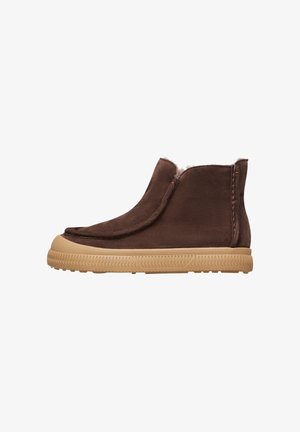 Bottines en daim marron avec une doublure en fourrure douce, une semelle en caoutchouc flexible et un design lisse et arrondi. Détails de couture sur les côtés visibles.