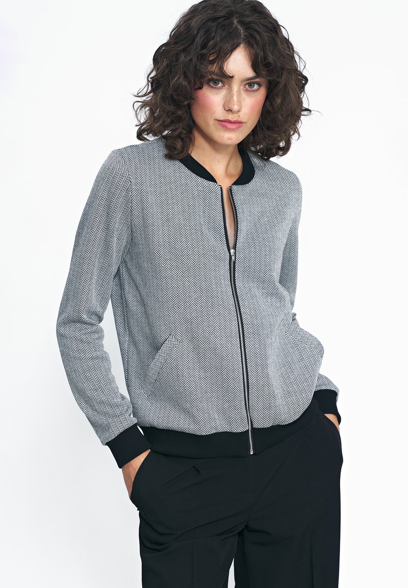 Czarna i biała bomberka w wzór houndstooth z zapięciem na zamek, bocznymi kieszeniami oraz jednolitymi czarnymi ściągaczami na mankietach i kołnierzu. Miękka tekstura.