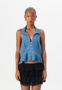 Denim top na halter z ovratnikom, z gumbom na sprednji strani in razširjenim robom; v paru z črno nabranimi mini krilom.