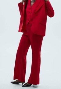 Roter, maßgeschneiderter Anzug mit einem doppelt geknöpften Blazer, einer taillierten Weste und ausgestellten Hosen. Glatter Stoff mit scharfen Revers und Taschen.