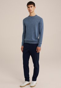 Kék környakú pulóver puha kötött anyagból, sötétkék nadrággal és fehér sportcipővel, amelynek világosbarna talpa van. Egyszerű és modern dizájn.