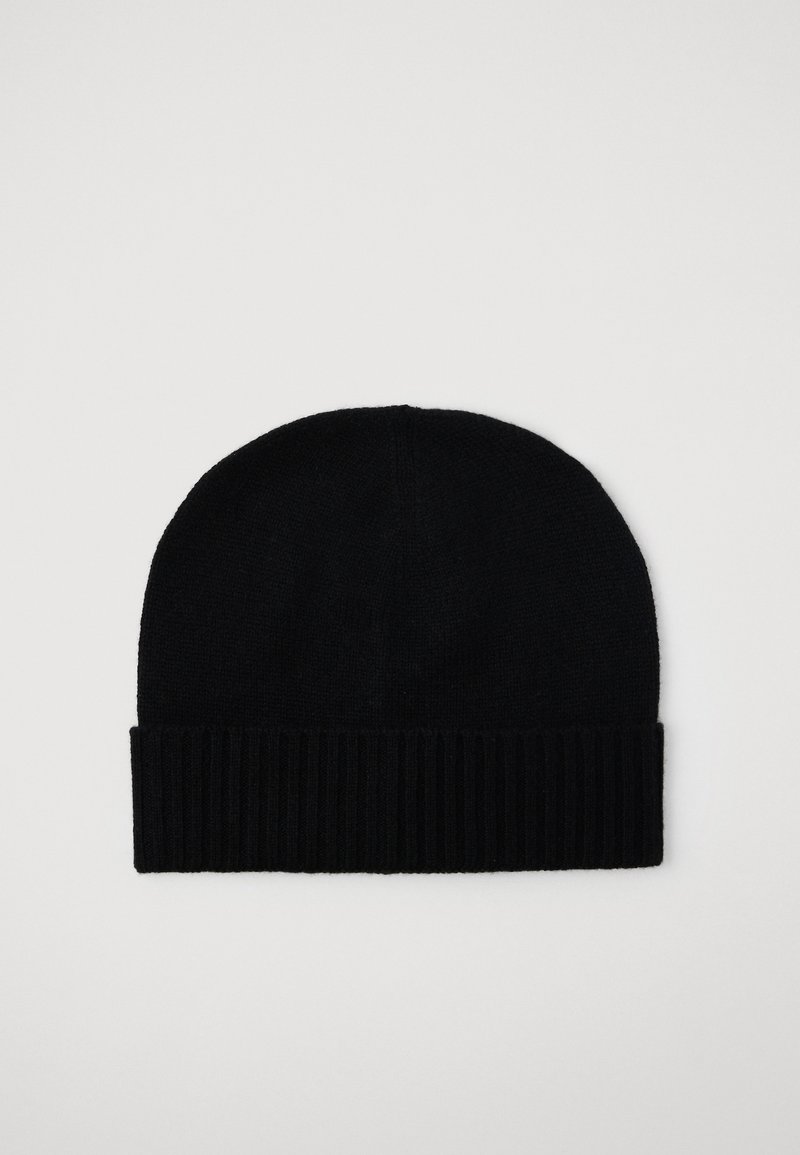 Gorro de lana negra trenzada con puño acanalado doblado sobre un fondo claro liso.