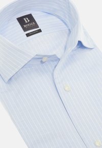 Chemise à rayures bleu clair en tissu lisse, avec un col classique, un devant à boutons et des boutons blancs. Étiquette de marque visible.