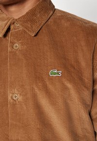 Corduroy shirt in brown, featuring a button-up design, vertical ribbing texture, and a green crocodile logo on the left chest.