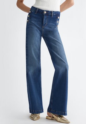 Jeans in denim blu a vita alta con taglio a gamba larga, caratterizzati da bottoni decorativi in argento sulla vita e una texture liscia.