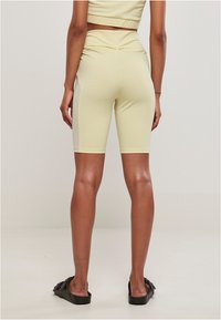 Shorts da ciclismo in tessuto elastico giallo con una texture liscia, vita alta e taglio aderente, abbinati a sandali neri a pianta piatta.