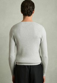 Pulover tricotat gri deschis, cu model în dungi, cu mâneci lungi, design ajustat și decolteu rotund, asortat cu pantaloni negri, văzut din spate.