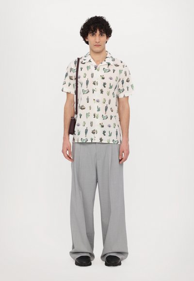 Camisa de mangas cortas con un fondo beige claro, que presenta varias plantas verdes y mariposas. Pantalones de pierna ancha grises, zapatos negros.