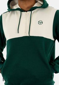 Sudadera verde y crema con diseño de media cremallera, que presenta un logo en el pecho. Fabricada con una tela suave y puños de canalé.