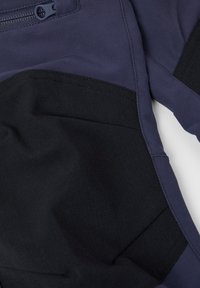 Kangasvaate tummansinisellä värillä mustilla yksityiskohdilla. Sisältää vetoketjullisen(taskun) ja teksturoituja paneeleita. Käytetyt materiaalit ovat sileitä ja kestäviä.