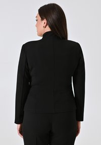 Zwarte op maat gemaakte blazer met een hoge kraag, lange mouwen en een slanke pasvorm, met een gladde textuur en een minimalistisch ontwerp.