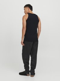 Débardeur noir ajusté, porté avec un pantalon sombre ample et des chaussures à enfiler. Le tissu semble doux avec une texture minimale.