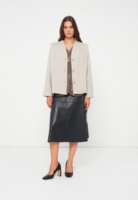 Blazer in lana grigia chiaro con taglio a quadrato, quattro bottoni, abbinato a una gonna midi in pelle scura e tacchi neri con design a tacco largo.