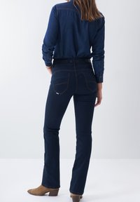 Jean en denim bleu foncé avec une silhouette ajustée, design à 5 poches et coutures contrastées, associé à une chemise en denim assortie.
