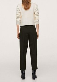 Crèmekleurige trui, met textuur en aangesloten pasvorm, gecombineerd met donker groene, op maat gemaakte broek met een rechte snit. Zwarte laarzen met hak maken de look compleet.