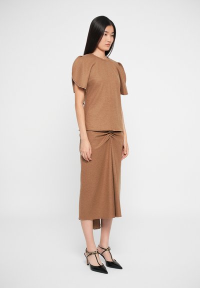 Top in maglia marrone con maniche a sbuffo abbinato a una gonna coordinata con dettaglio torcido, completato da eleganti tacchi a punta neri.